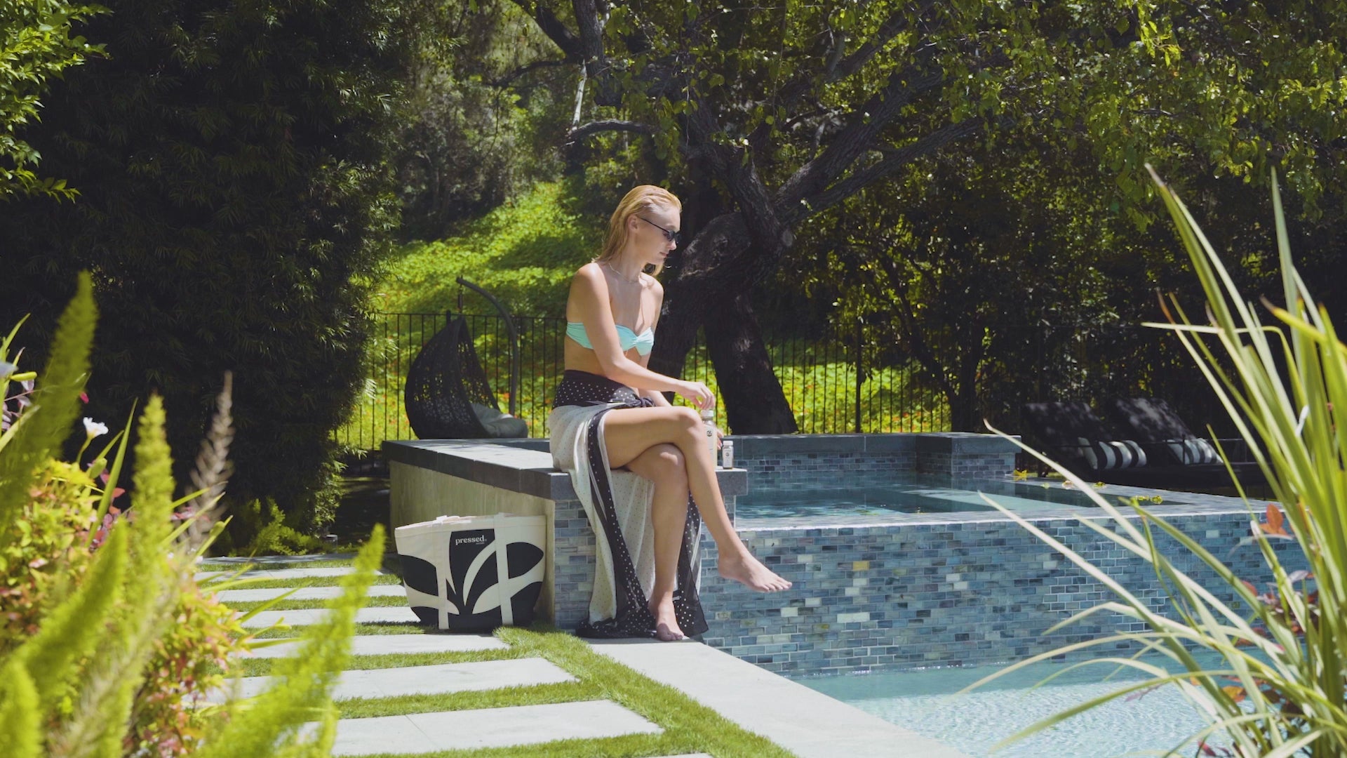 In a sunny poolside setting, a woman opens and drinks a Pressed Simple Cleanse juice and Debloat Shot. The video ends with both Vacation Prep Pack products displayed beside the pool.